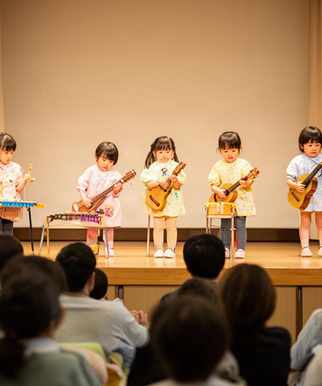 発表会の舞台で楽器を演奏する園児と客席の保護者